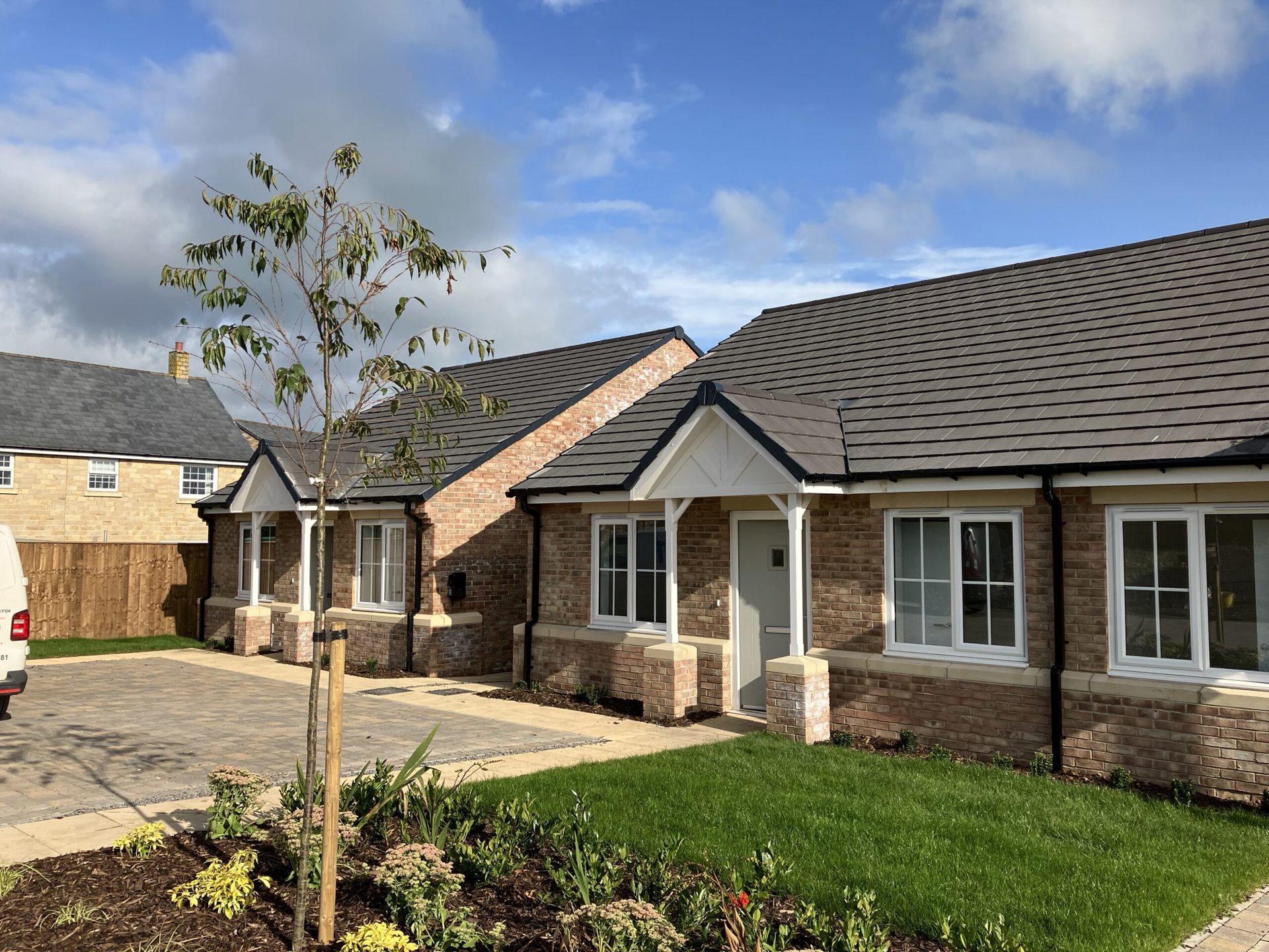 two newly built bungalows with light bricks and slate roofs. They have a small garden and driveway.