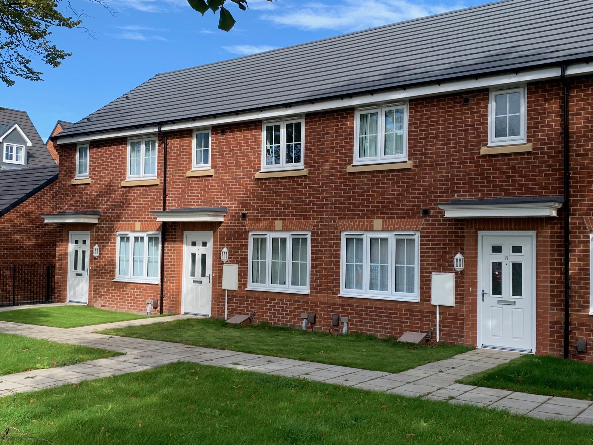 Red brick terraced houses with white windows and doors and a small front garden.