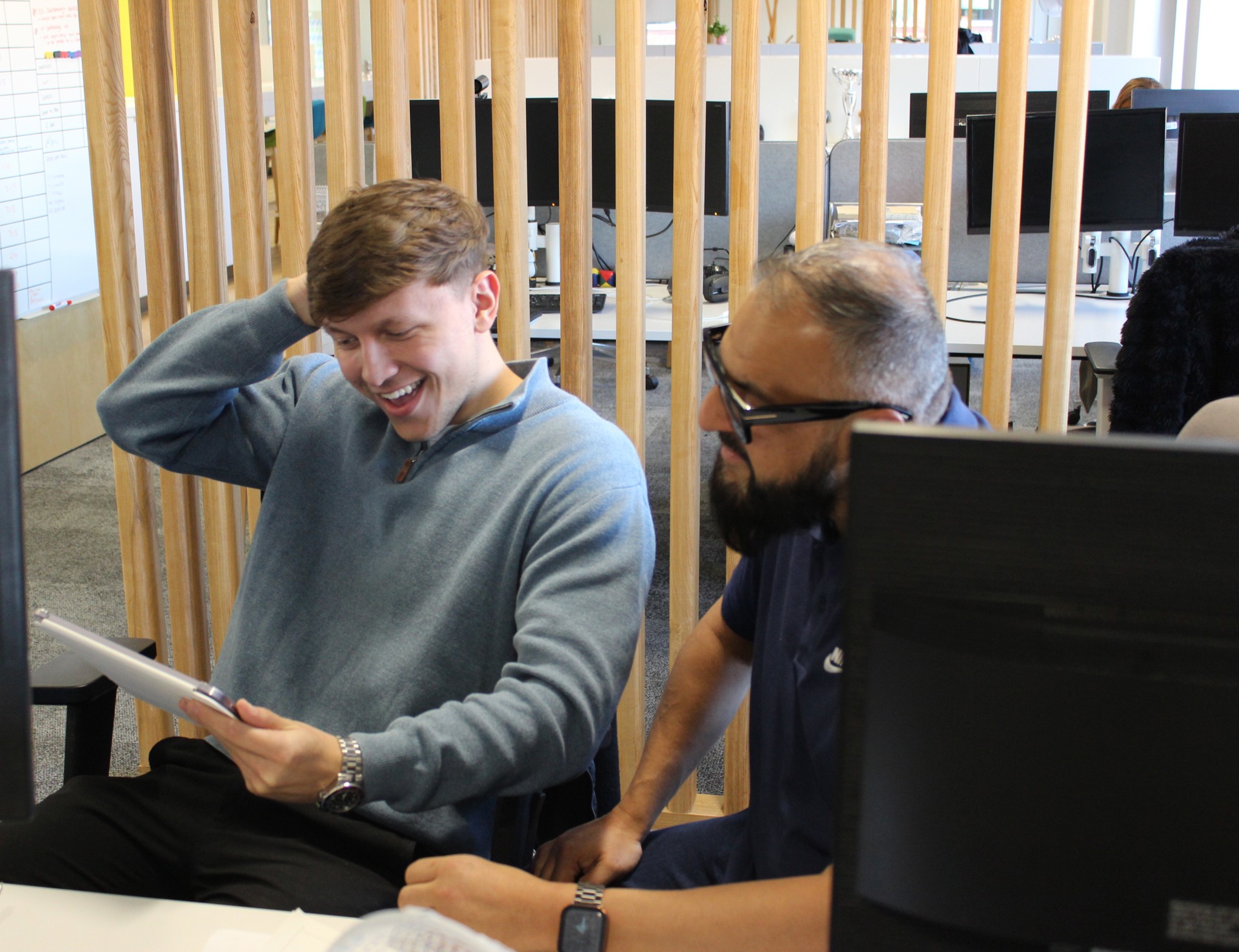 Two people sat looking at an electronic tablet in an open, airy office space.