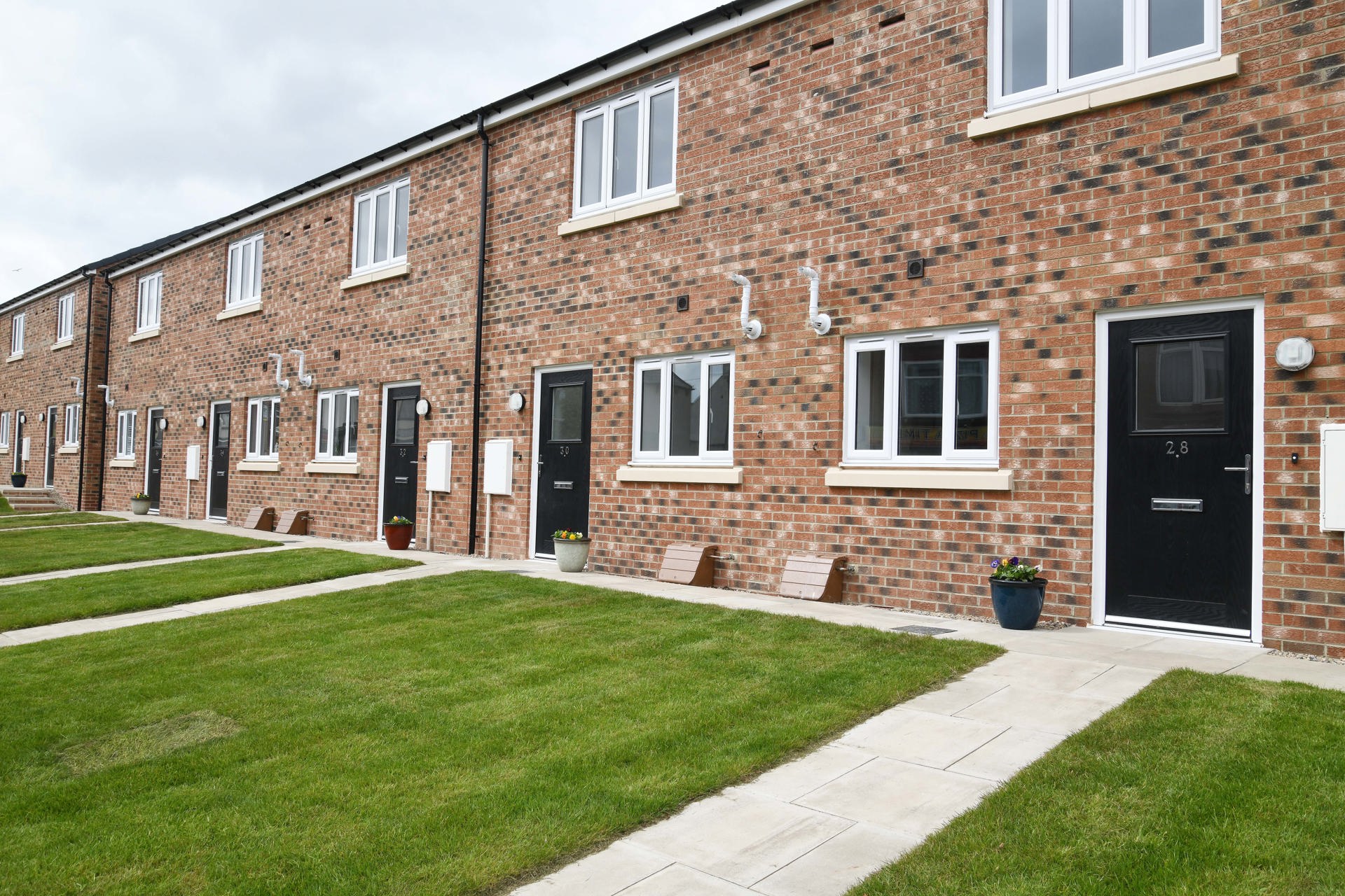 A row of terraced houses with light brick, black door and a lawn in front of the door.