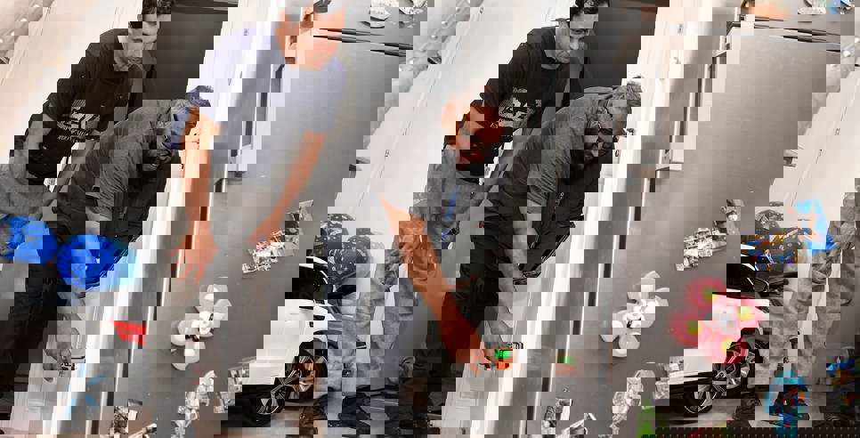 A housing officer uses a handheld device to inspect a wall inside a home, while the resident watches closely. They are in a kitchen area with a fridge covered in magnets and children’s toys visible in the background.  Let me know if you want a version tailored for accessibility compliance or a shorter version for web use.